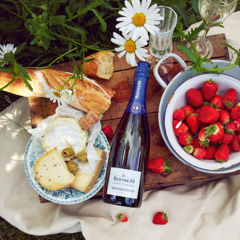 Crémant d’Alsace Bestheim Extra Brut Chardonnay sur une nappe de pique-nique, avec fromages et fraises