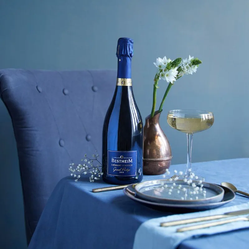 Crémant Bestheim Grand Prestige sur une table dressée en bleu, à côté d’une coupe