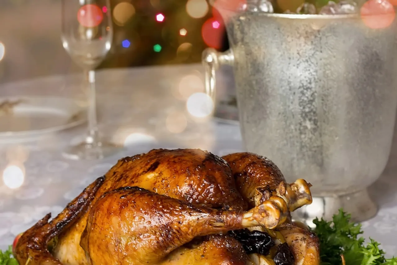 Volaille rôtie dorée sur une table de fête, avec une flûte et un seau à champagne devant les lumières de Noël